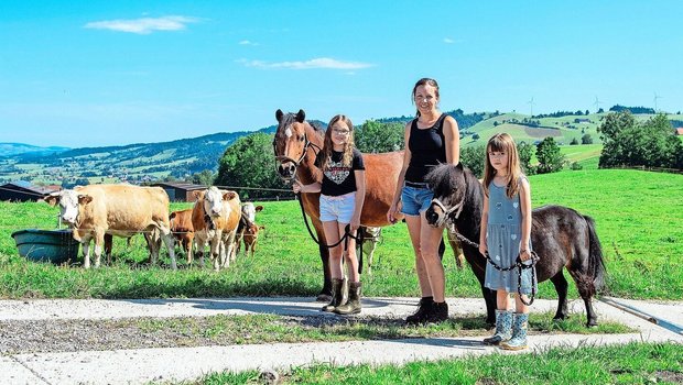 Larissa mit ihrem Pony Dino, Martina Wicki und Lea mit dem Shetty Leni. Die betriebseigenen Simmentaler-Mutterkühe mit ihren Kälbern beobachten die Szene.